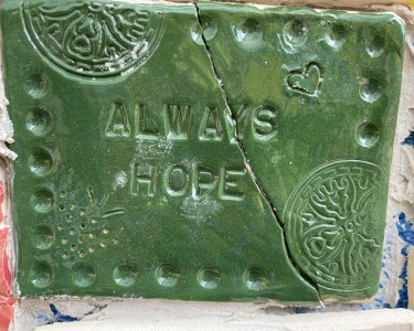 a green ceramic tile with a diagonal crack, reading "Always Hope"
