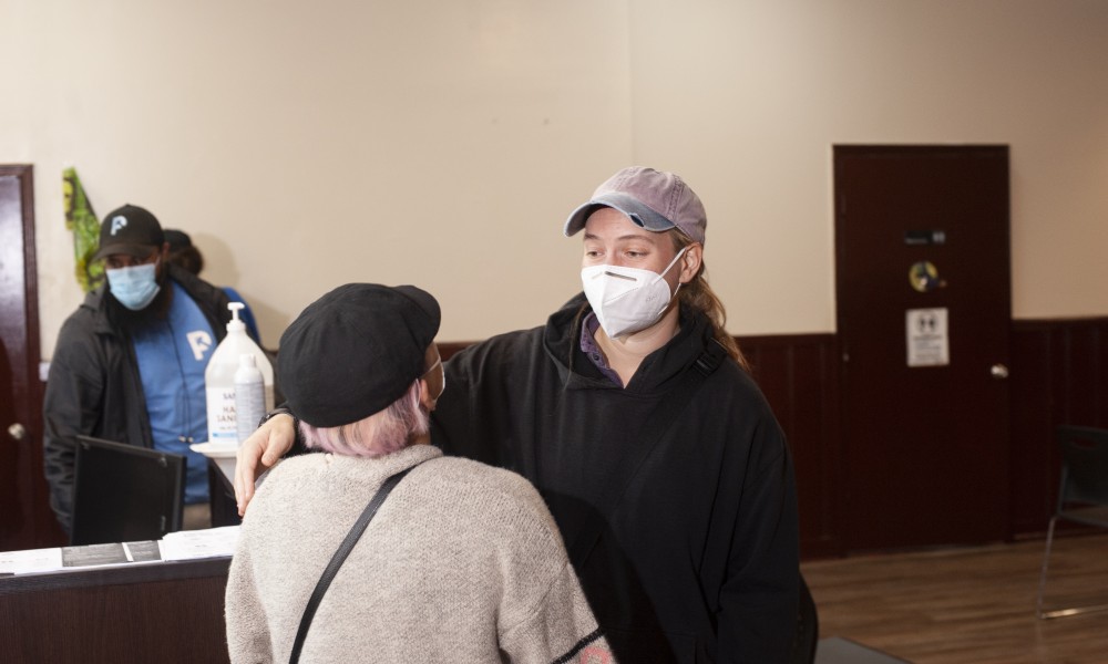 Two women in masks speaking, looking happy.