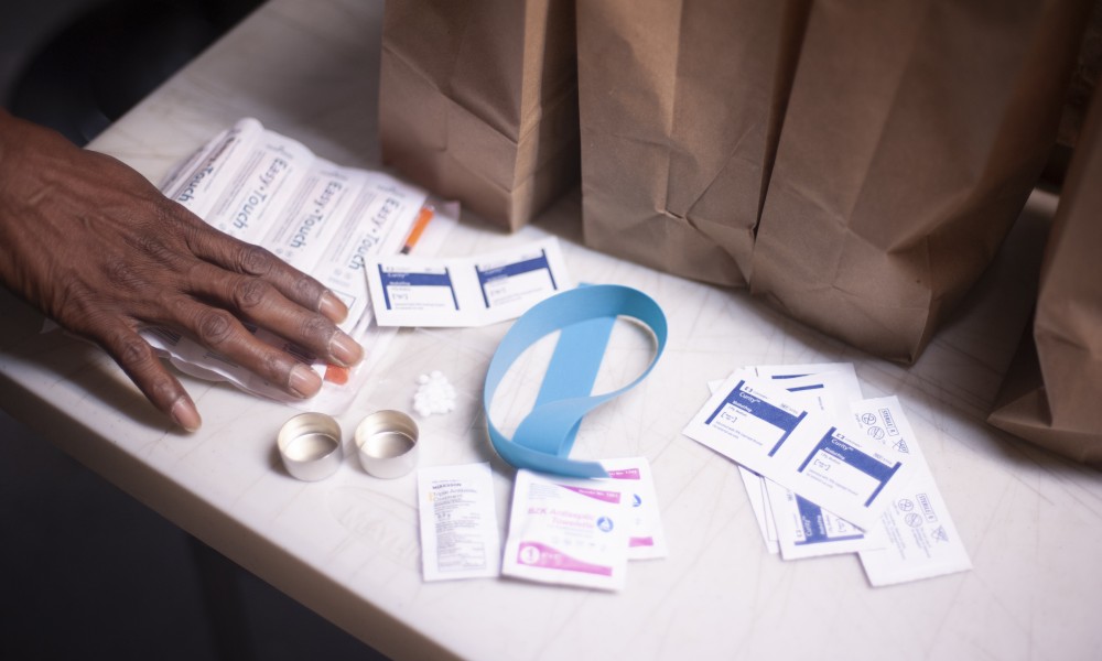 A hand gesturing towards Syringe Service supplies including alcohol wipes, tourniquet, cookers, and syringes.