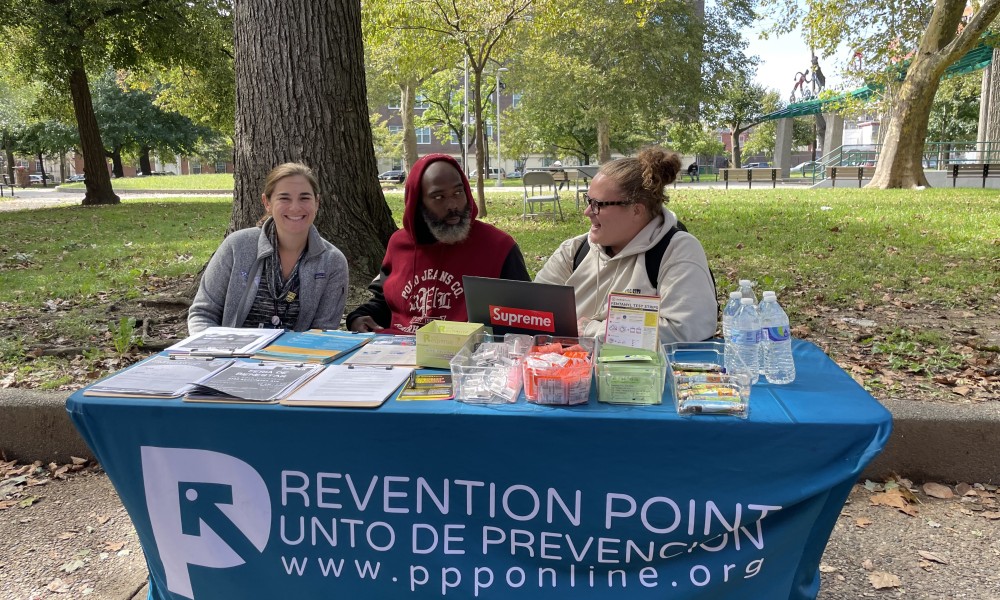 Three people sitting at a Prevention Point table: a doctor, a prospective participant, and Nicky. 