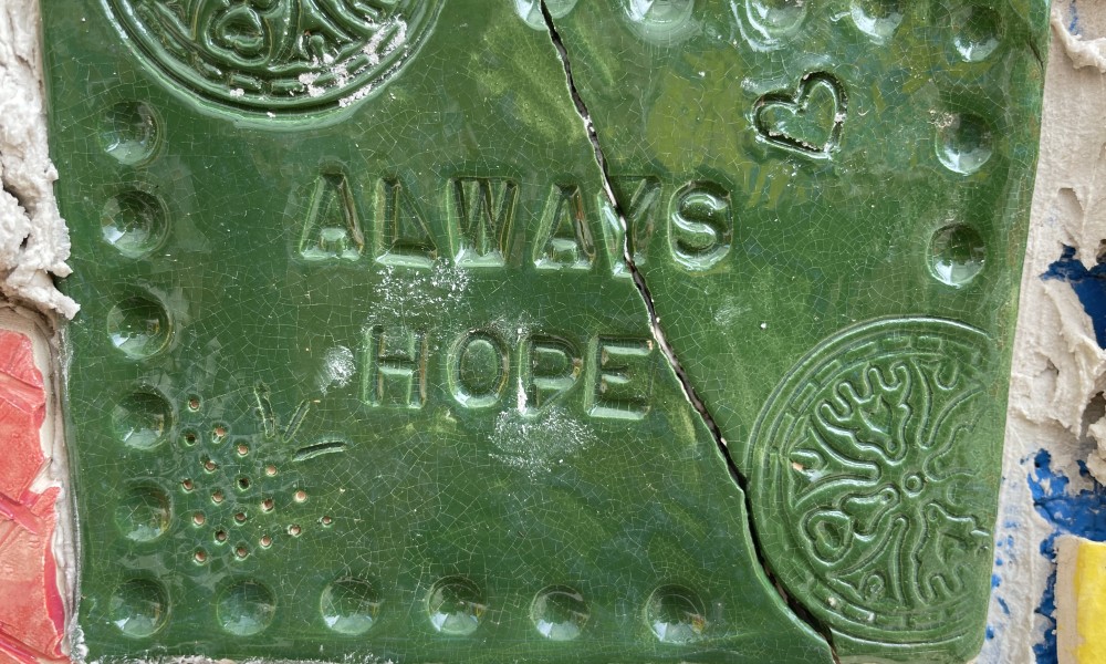 a green ceramic tile with a diagonal crack, reading "Always Hope"