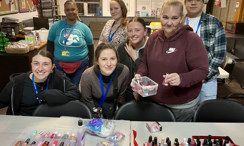 Seven staff and volunteers look at the camera with nail polish displayed in the foreground