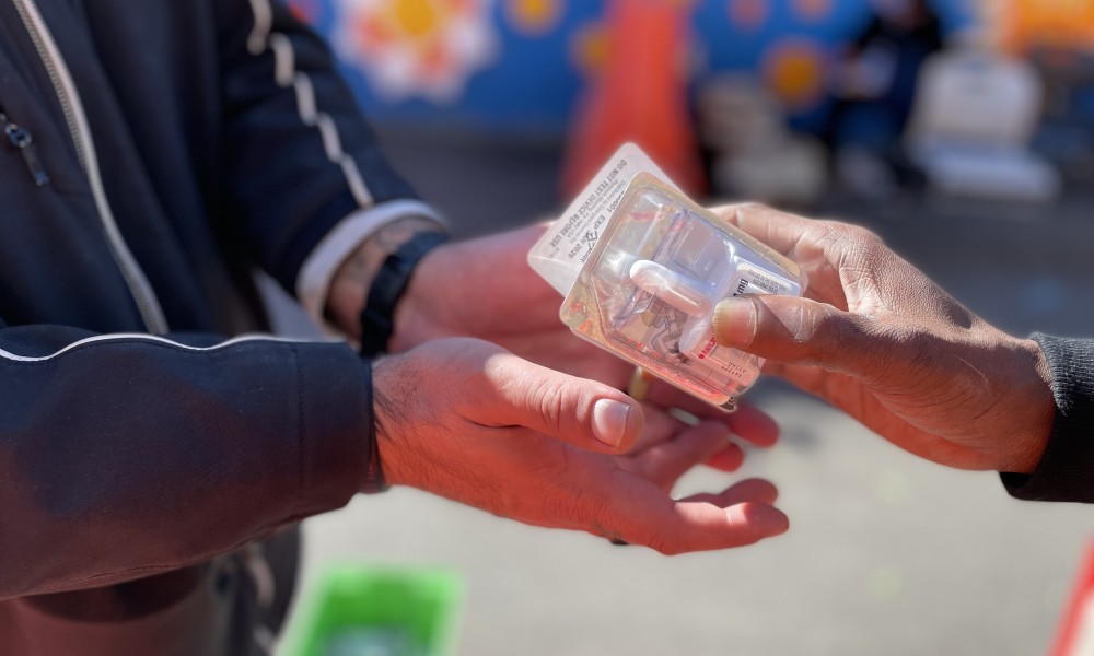 one hand puts two doses of Narcan in someone else's cupped hands.