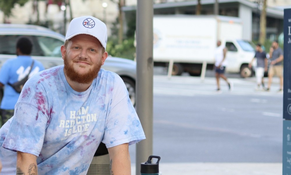 James wears a tie dye shirt that reads, "Harm reduction is love."