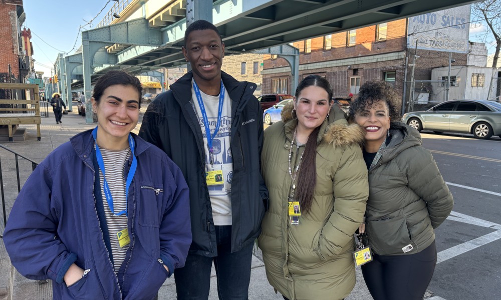 four staff stand outside next to the street with a train track running overhead. They're smiling at the camera.