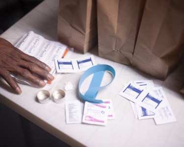 A hand gesturing towards Syringe Service supplies including alcohol wipes, tourniquet, cookers, and syringes.