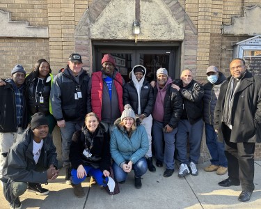 Twelve people pose and smile at the camera. It's the mobile bus team and community members, including a local pastor. 