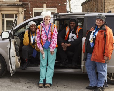 four people smile from a van
